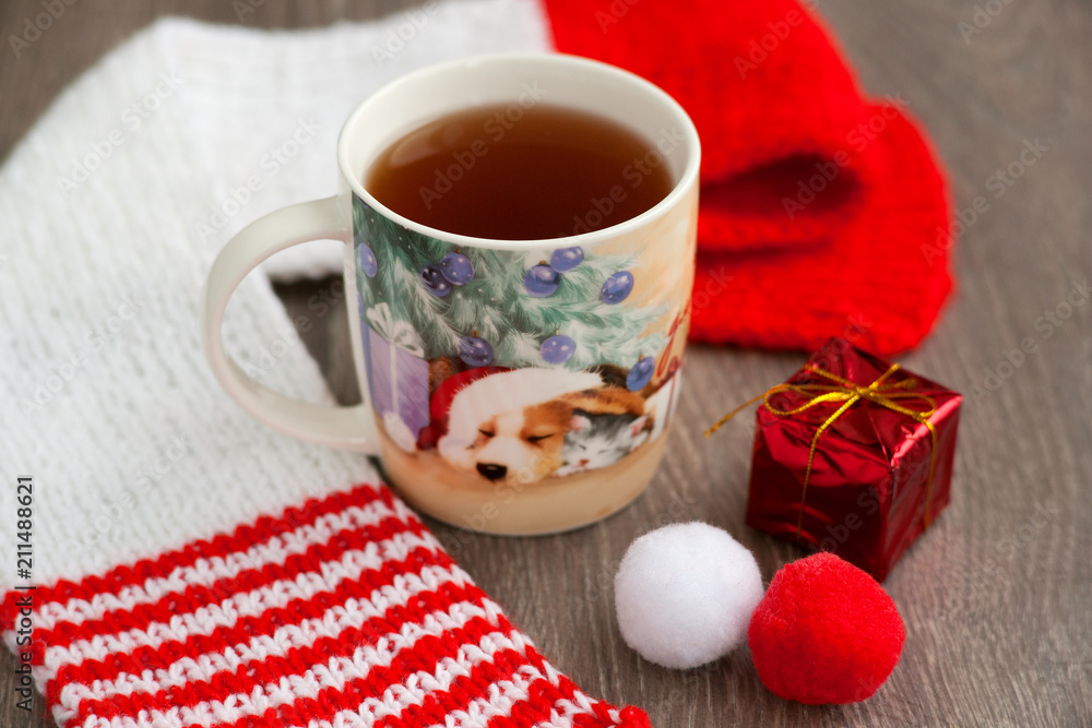 Tea in the New Year's mug. Image of a dog on a mug of tea, as a symbol of the year of the dog. Tea in the new year, red knitted scarf, Santa's cap create a New Year mood. New Year's dog. Tea in the New Year's mug. Image of a dog on a mug of tea, as a symbol of the year of the dog. Tea in the new year, red knitted scarf, Santa's cap create a New Year mood. New Year's dog.