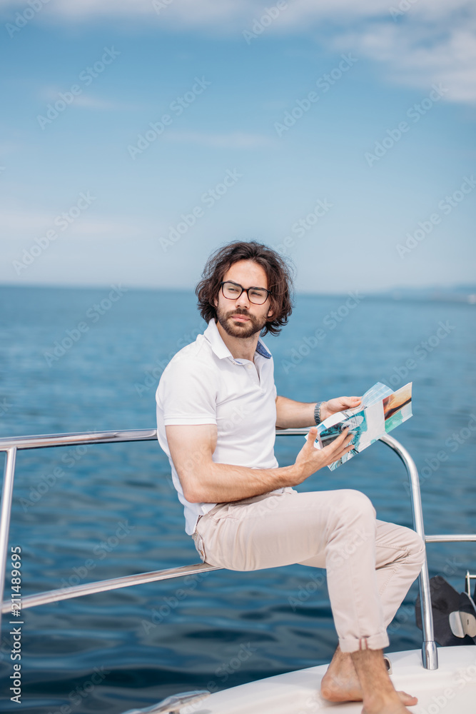 Obraz premium Young bearded man on a luxury yacht with a magnificent view of the sea. Sailing. Luxury yachts. Summer vacation and voyage concept.