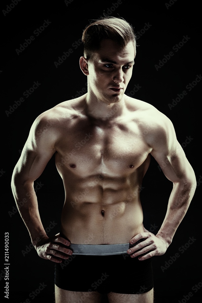 Handsome sporty young man in underwear posing on dark background