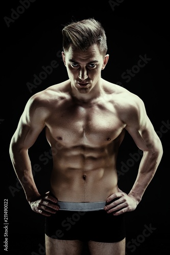 Handsome sporty young man in underwear posing on dark background