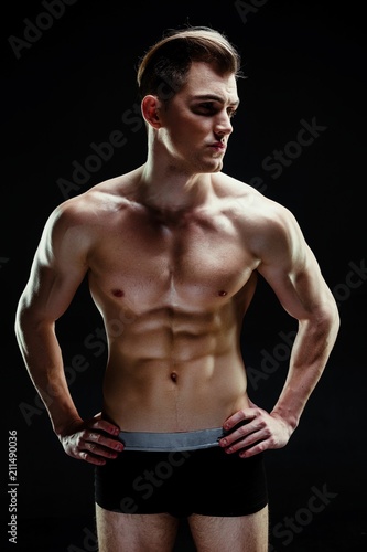 Handsome sporty young man in underwear posing on dark background