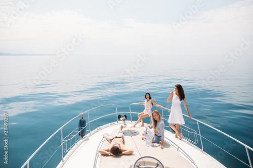 Young friends resting on bow of boat spending time together, enjoying sun bathing. Baner. Outdoor shot with blue marine background. Concept of vacation or holiday. © alfa27