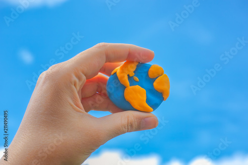 Woman holding planet Earth in her hand against blue sky