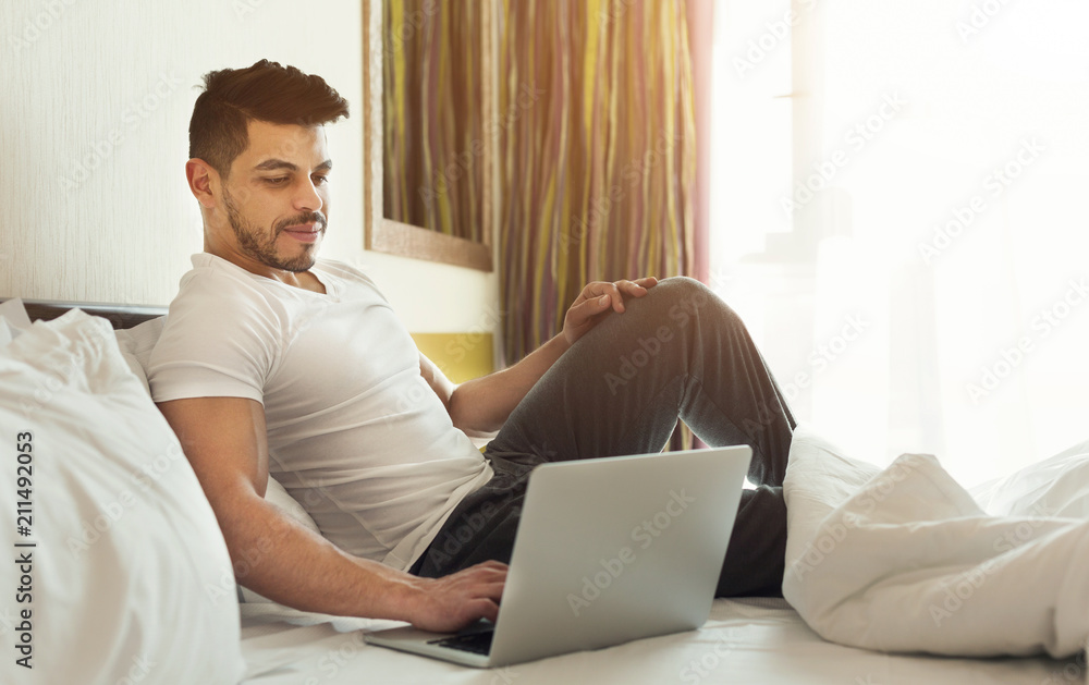 Young man using laptop while sitting on a bed Young man using laptop while sitting on a bed
