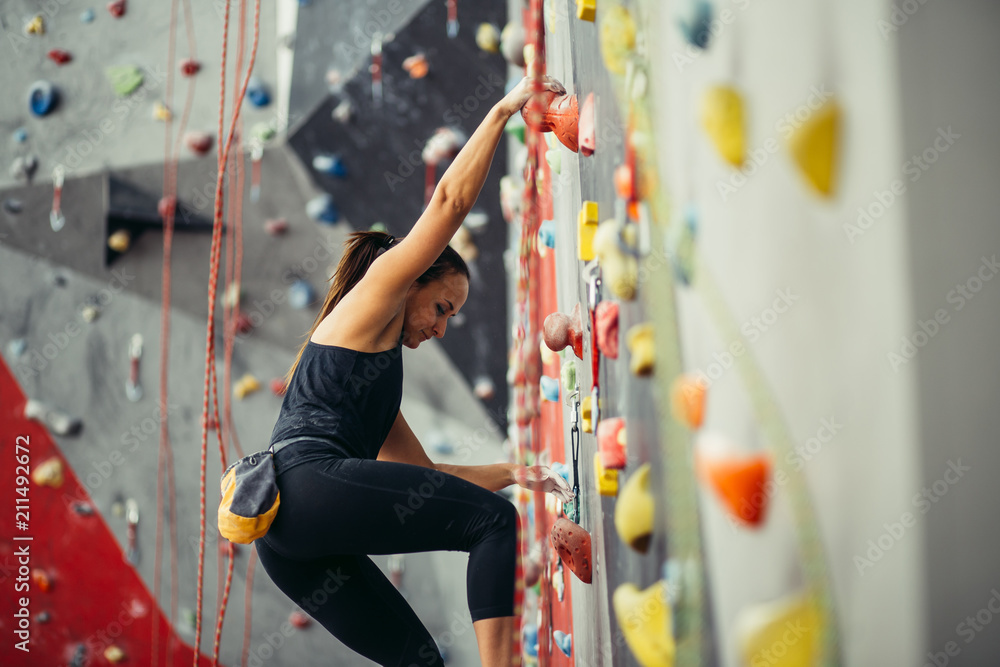 Side view of athletic woman practicing rock climbing on artificial wall  indoors. Active lifestyle and bouldering concept. Stock Photo