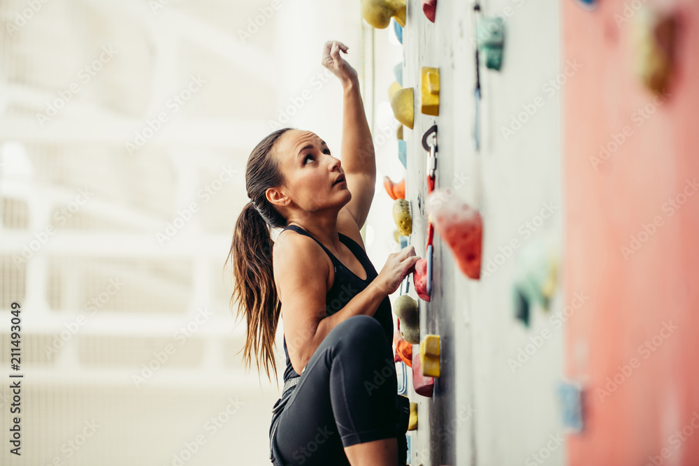 Side view of professional climber female at the rock climbing wall at the gym. Light background with copyspace - obrazy, fototapety, plakaty 