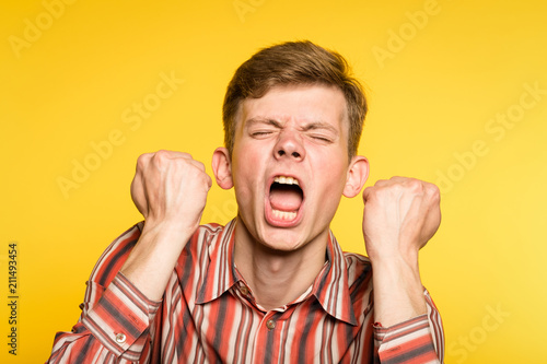 tantrum hysterics. man has a hysterical fit screaming. emotion facial expression and feelings. portrait of a young guy on yellow background. photo