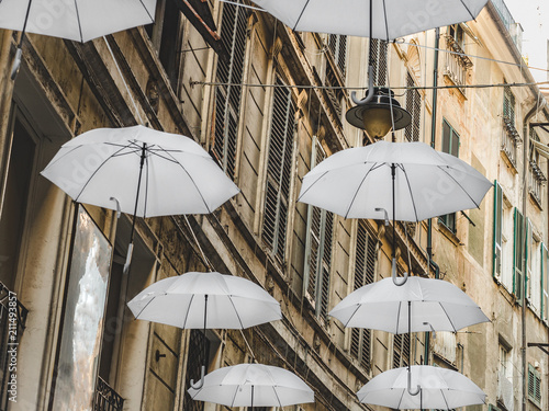 Multicolored, bright umbrellas hanging between houses on the beautiful, narrow streets of the magnificent city of Genoa against the blue sky, on a sunny, summer day. Concept of travel and recreation