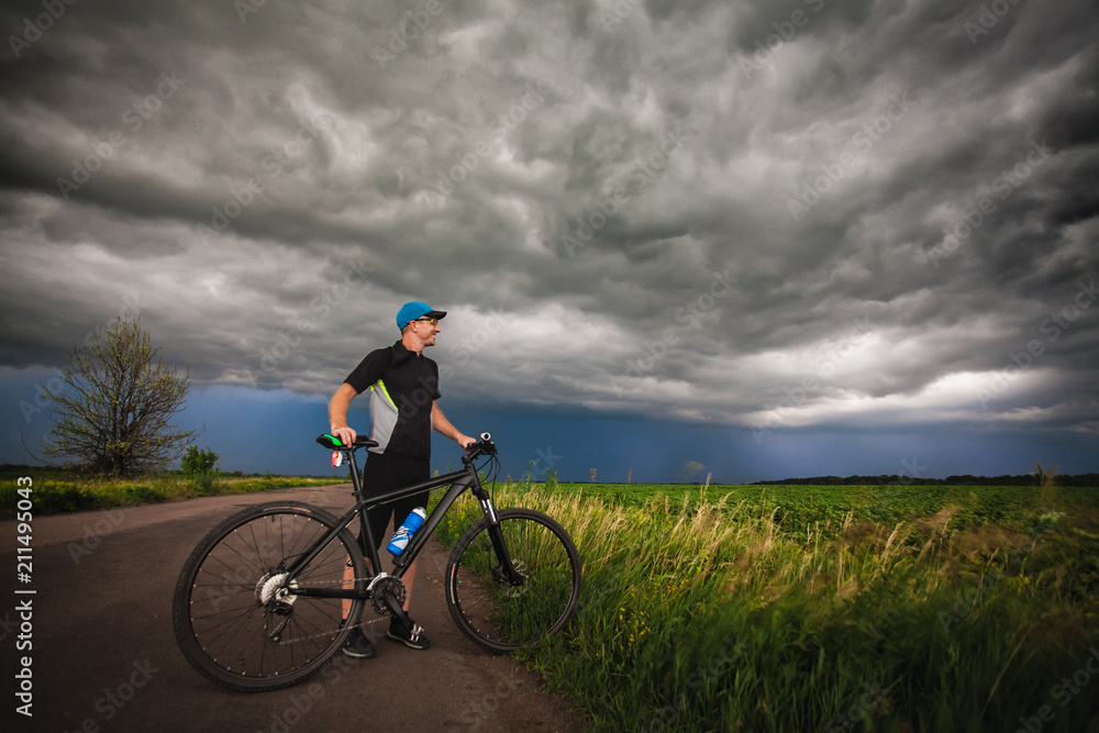 Happy man cyclist rides field road on a mountain bike. before the storm