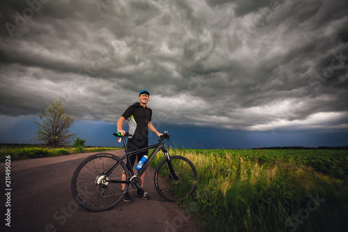 Happy man cyclist rides field road on a mountain bike. before the storm © Dmytro Titov