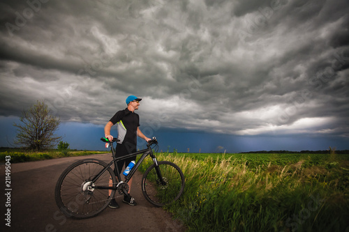 Fototapeta Naklejka Na Ścianę i Meble -  Happy man cyclist rides field road on a mountain bike. before the storm