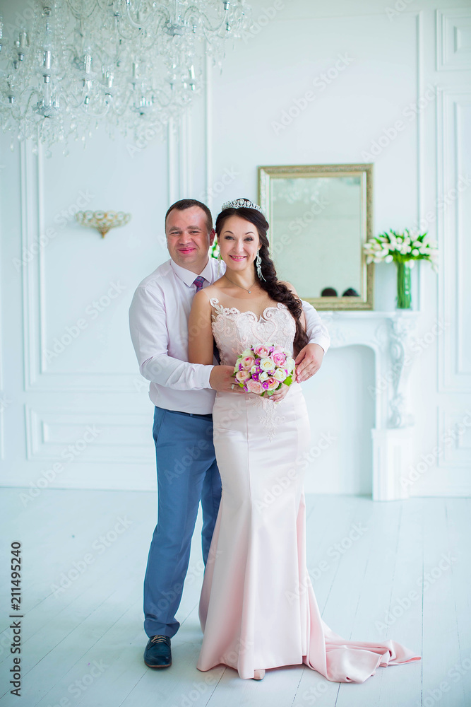 Groom tenderly embraces lovely bride on background of white room with fireplace and mirror Groom tenderly embraces lovely bride on background of white room with fireplace and mirror