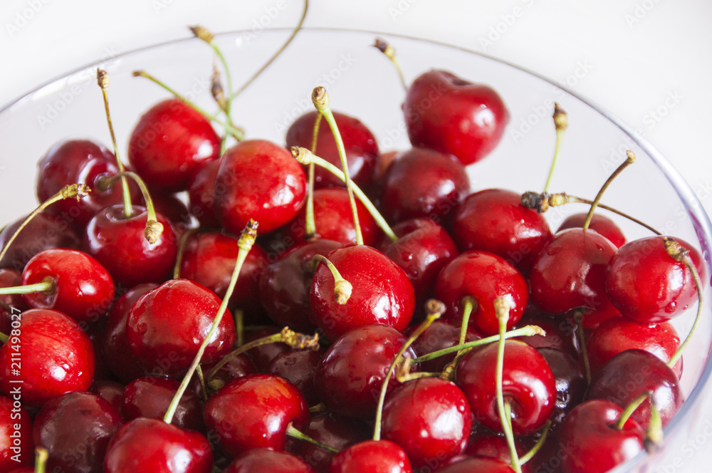 Ripe cherries in glass bowl on white fabric background Ripe cherries in glass bowl on white fabric background