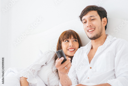 An attractive young couple lying in bed and watching movie.