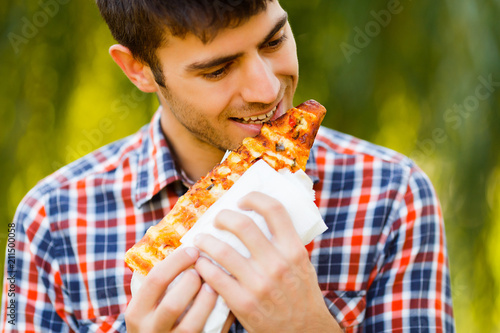 Cheerful young guy is eating pizza on the park photo