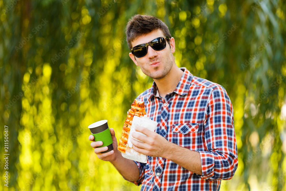Man eating pizza. Cheerful young guy is eating pizza drinking coffee on the park Man eating pizza. Cheerful young guy is eating pizza drinking coffee on the park