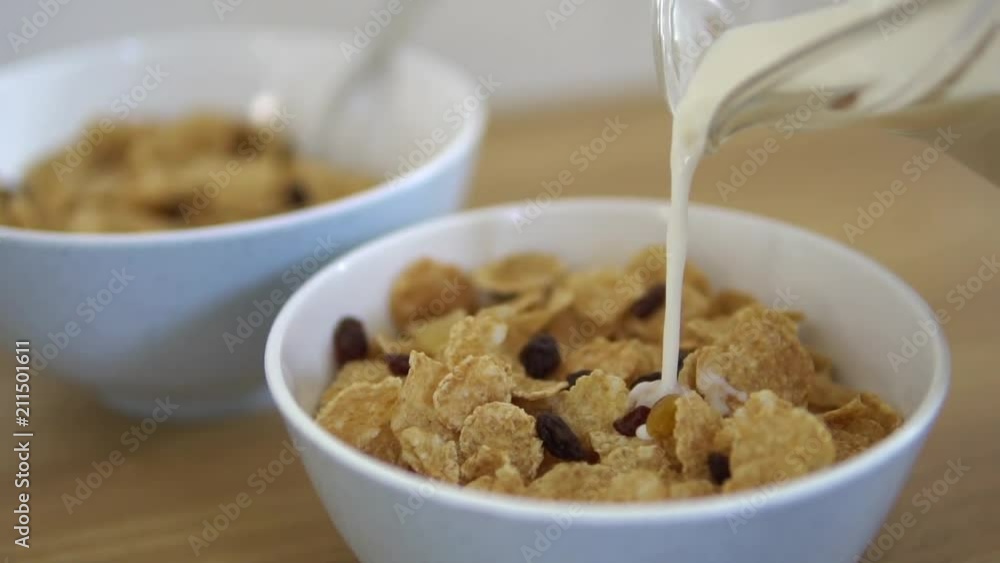 Fresh and healthy caw milk slowly pouring in the white bawl. Healthy food and flakes at the background. Serving breakfast from quality products ( flakes and oat ) as the healthy meal for morning. Fresh and healthy caw milk slowly pouring in the white bawl. Healthy food and flakes at the background. Serving breakfast from quality products ( flakes and oat ) as the healthy meal for morning.
