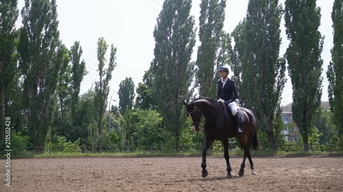 young girl riding a strong brown horse outdoors sand parkour dressage arena at dawn. Competitive training of riders. A woman in the festive uniform of a rider. sliding camera movement to the left. the photo