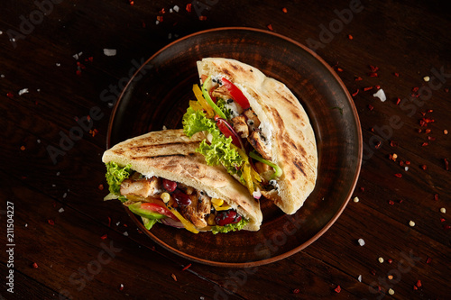 Pita stuffed with chicken, beans and letucce on clay plate over wooden background, top view, selective focus.