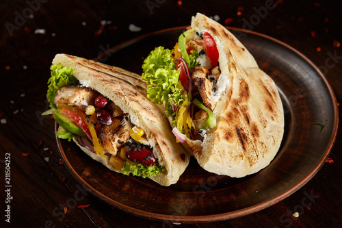 Pita stuffed with chicken, beans and letucce on clay plate over wooden background, side view, selective focus.