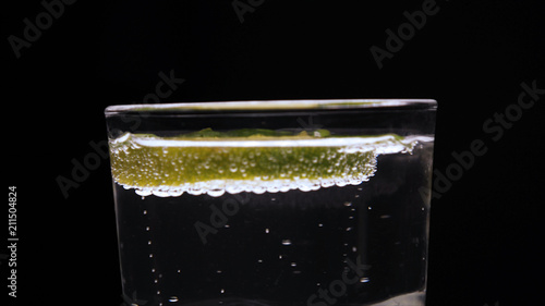 Carbonated water in a transparent glass, lime, bubbles, black background.