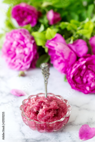 Jam with rose petals in a glass bowl and bright roses on a light background.
