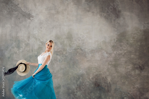 Beautiful young woman in a lush blue skirt, whirling and dancing. Summer style, straw hat with black ribbon.