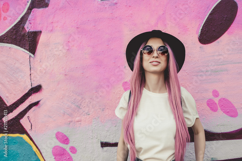 Szczęśliwy szykowny młody hipster kobieta z długie różowe włosy, kapelusz i okulary przeciwsłoneczne na ulicy.