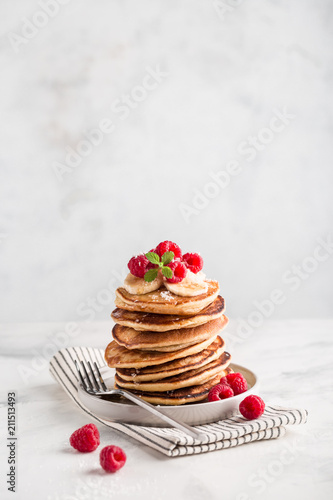 Stack of homemade pancakes with fresh raspberries on light concrete background, copy space