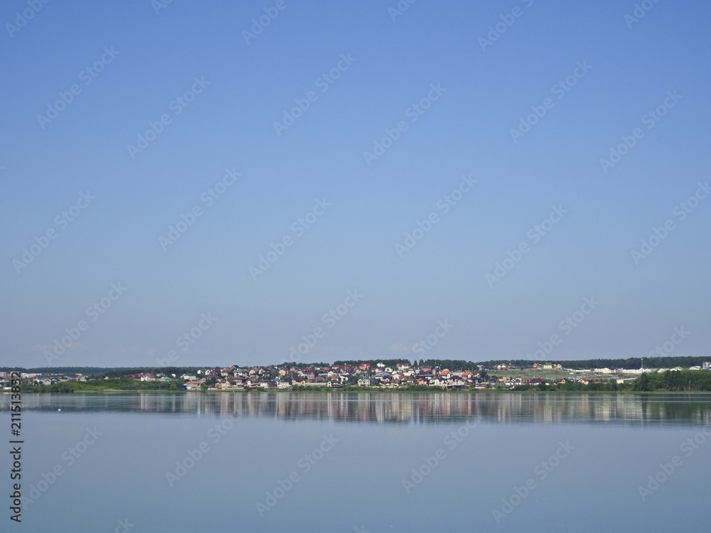 Panorama of the village against a calm lake and a blue cloudless sky