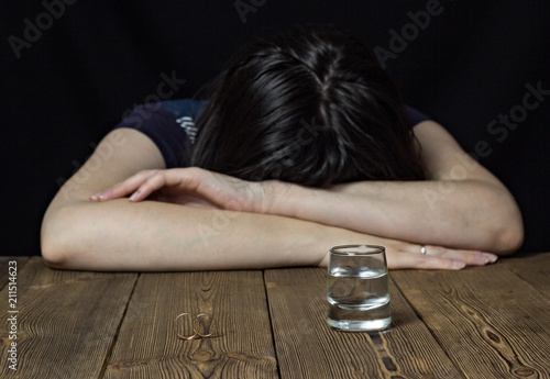 Canvastavla Drunk girl and alcohol on a wooden background, wedding rings on a table, divorce