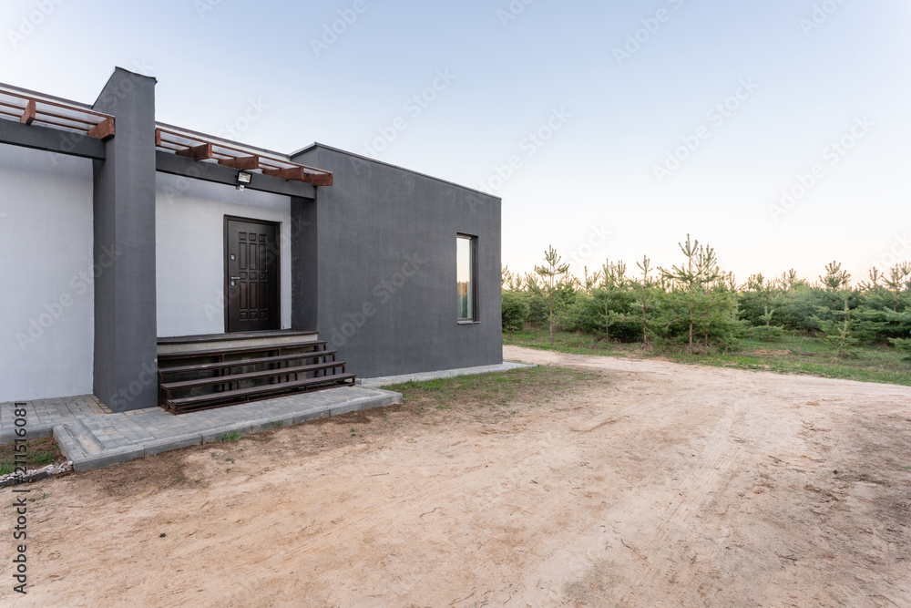 Side view of an open veranda in front of a modern forest cottage. Pine young forest under the sunset rays in the background. Side view of an open veranda in front of a modern forest cottage. Pine young forest under the sunset rays in the background.