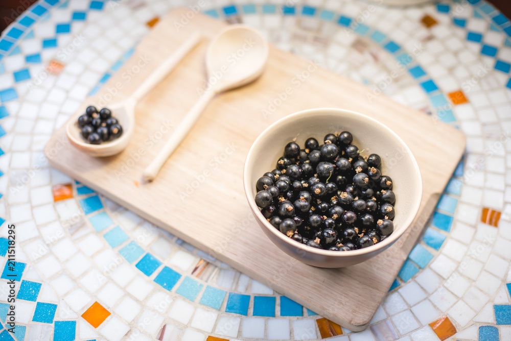 A plate of black currant and a wooden spoon on a table. A plate of black currant and a wooden spoon on a table.