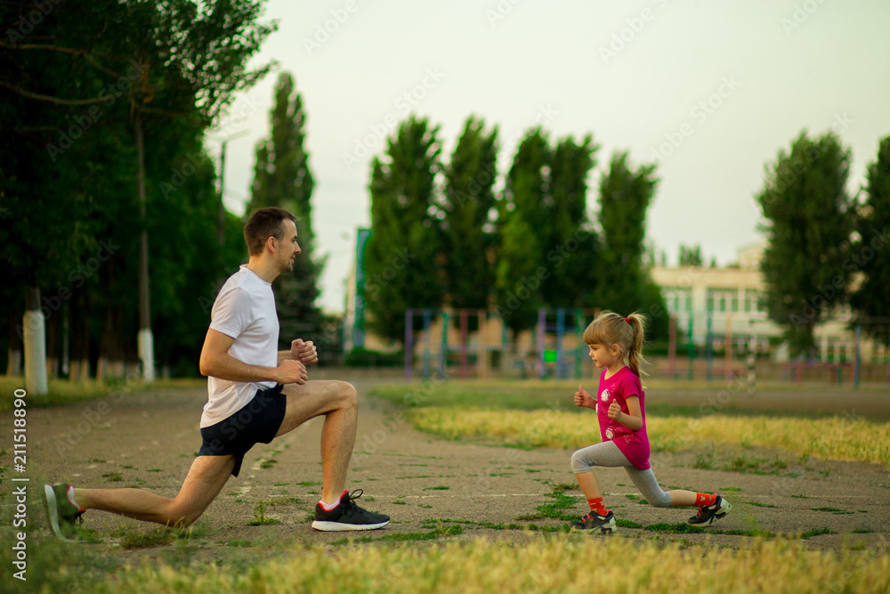 Athletic young father and little daughter do exercises in nature. Healthy lifestyle