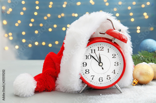 Alarm clock with Santa hat and festive decor on table. Christmas countdown