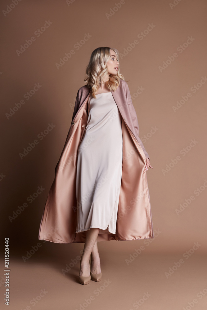 Beautiful blonde woman posing in a pink coat on a beige background. Fashion show clothing, woman with perfect figure, long hair. Trendy fashionable autumn coat on the girl's body Beautiful blonde woman posing in a pink coat on a beige background. Fashion show clothing, woman with perfect figure, long hair. Trendy fashionable autumn coat on the girl's body