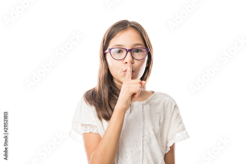 Beautiful little girl putting finger up to lips & ask silence on white background
