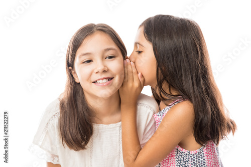 Younger sister whispering gossip to her elder sister on white background
