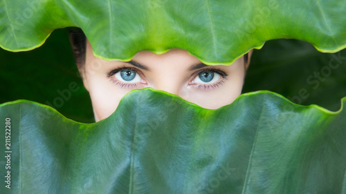 Young woman's face surrounded by tropical leaves.