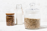 glass jar with oat flakes, granola and bottle of milk, closeup