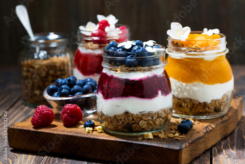 breakfasts in jars with muesli, berry puree and cream on wooden board