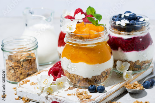 desserts with granola, berry and fruit puree in jars on white wooden board, closeup