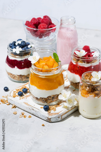 desserts with muesli, berry puree and fruit in jars on white table, vertical