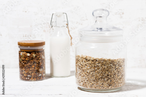 glass jar with oat flakes, granola and bottle of milk, closeup