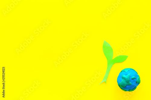 Planet, ecology. plastiline symbol of planet Earth globe and plant coutout on yellow background top view space for text
