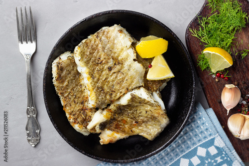 Canvas Print Fried cod fish fillet with spice in a cast iron pan. Top view.