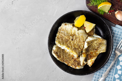 Canvas Print Fried cod fish fillet with spice in a cast iron pan. Top view.