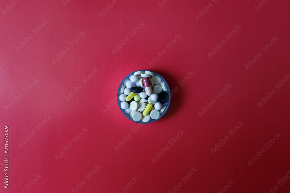 Assorted pharmaceutical medicine pills, tablets and capsules on red background