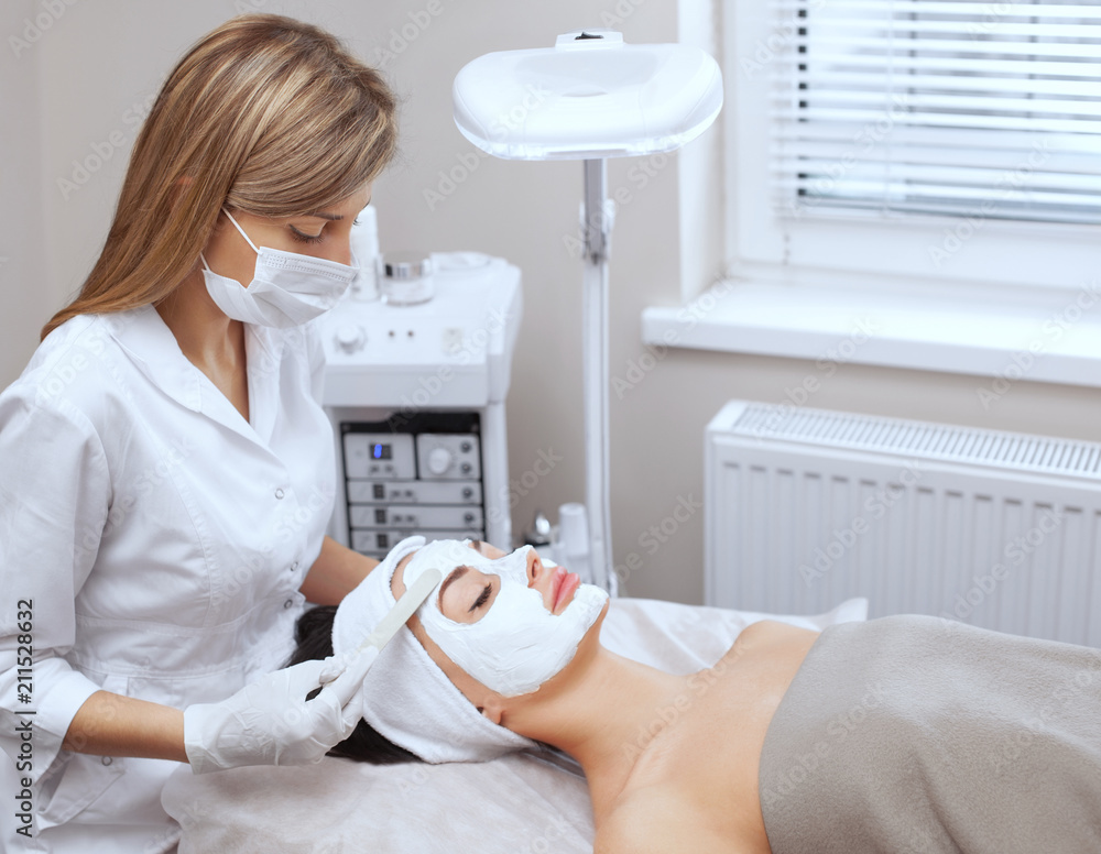 The cosmetologist for the procedure of cleansing and moisturizing the skin, applying a mask with stick to the face of a young woman in beauty salon. Cosmetology and professional skin care. The cosmetologist for the procedure of cleansing and moisturizing the skin, applying a mask with stick to the face of a young woman in beauty salon. Cosmetology and professional skin care.
