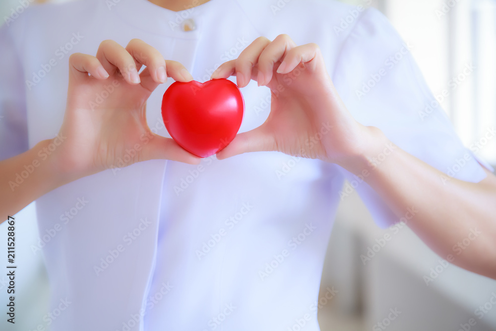 Red heart held by smiling female nurse's hand, representing giving effort high quality service mind to patient. Professional, Specialist in white uniform concept